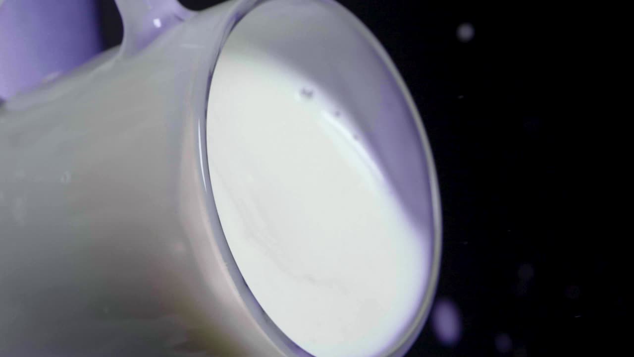 Ripresa statica verticale di latte d'avena vegano in un bicchiere con una fragola che schizza al rallentatore, su sfondo nero