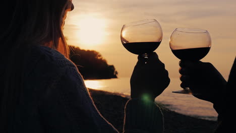 silhouettes of a young couple drinking wine at sunset on the shore of the lake 2