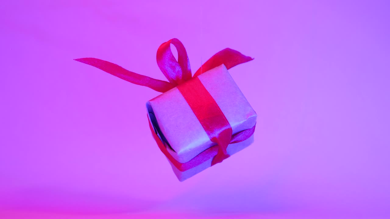 caja de regalo con cinta roja girando sobre fondo púrpura de neón. rotación de 360 grados. bucle sin costuras. gravedad cero. levitación. ventas de concepto, precio de descuento, vacaciones de navidad y compras