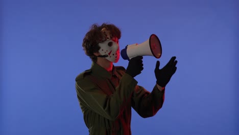 man in white mask with loudspeaker in hands on blue background with red neon light image of maniac - man in white mask with loudspeaker in hands on blue background with red neon light. image of maniac jason voorhees from friday 13. he is saying something. halloween celebration concept