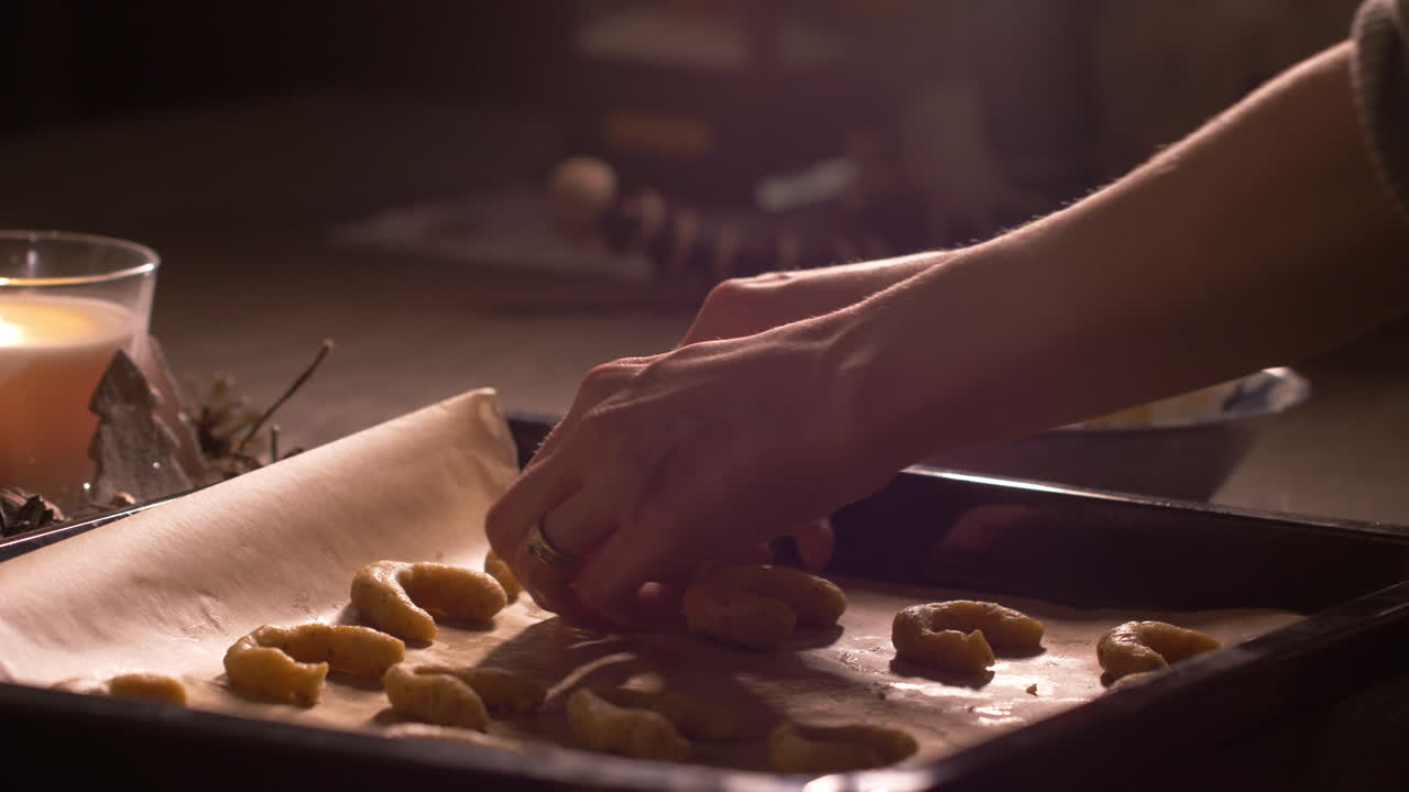 Woman baker's hands sorting raw crescent shape cookie dough on oven baking tray