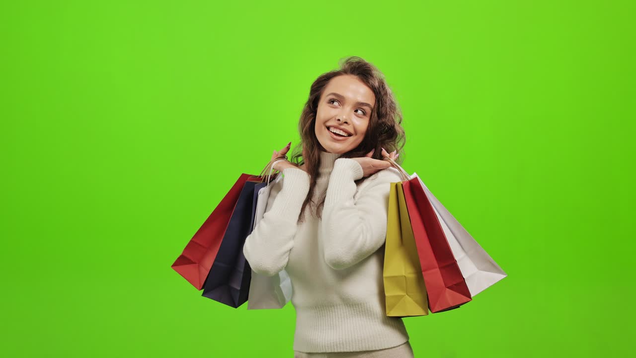 그 여자는 카메라를 바라보고 미소 짓고 쇼핑백을 들어올리며 매우 행복합니다.그녀는 녹색 배경에 서 있습니다.녹색 화면.