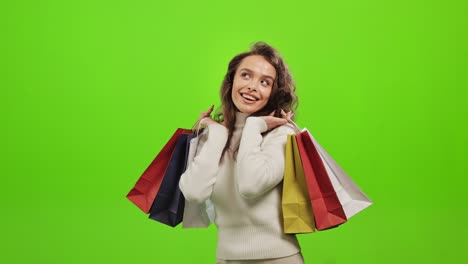 la mujer está mirando a la cámara y sonriendo. está levantando las bolsas de compras. está muy feliz. está de pie sobre un fondo verde. pantalla verde. 4k.