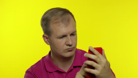 Young-caucasian-man-posing-in-pink-t-shirt.-Handsome-guy-using-mobile-phone-and-win-something