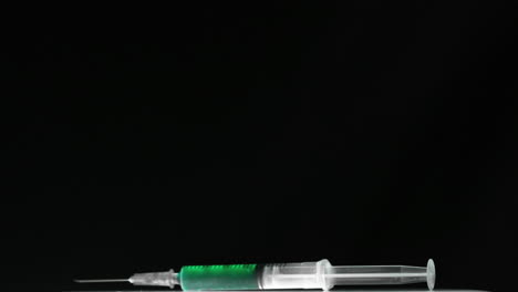 Syringe-of-green-liquid-falling-and-bouncing-on-black-surface