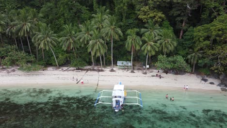 Luftaufnahme-Der-Pasandigan-Bucht-In-El-Nido-Und-Urlauber-Auf-Einem-Inselhüpfer-Tourboot,-Die-Sich-Am-Sandigen-Palmenstrand-Inmitten-Tropischer-Landschaft-Entspannen