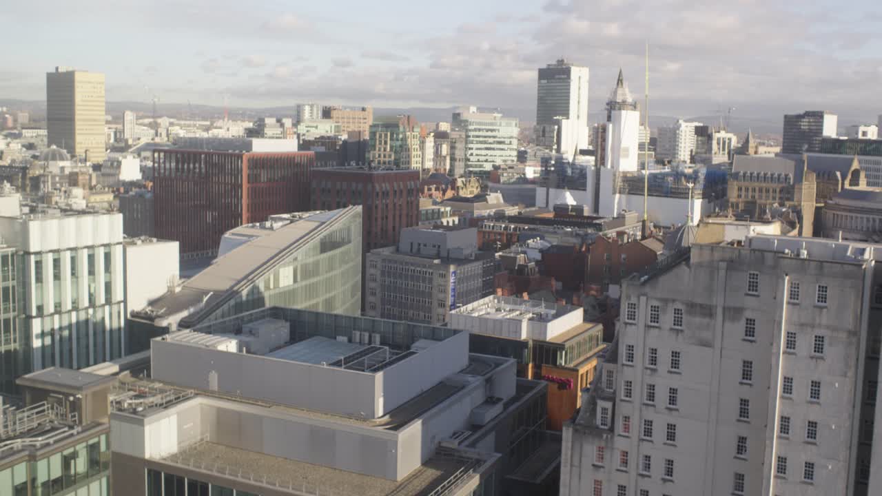 Slow pan across Manchester City centre, at the heart of its financial district, with a view of the hills at the city's edge in the background.