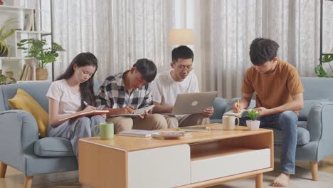 asian teen group studying at home, doing a project, writing into notebook, a boy in white t-shirt typing on laptop