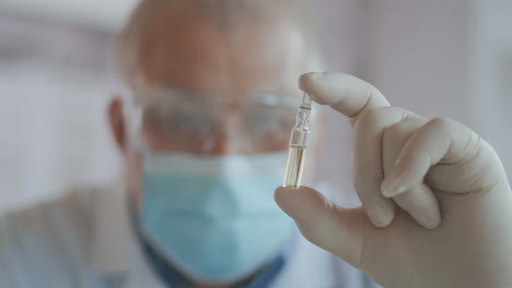 close-up a masked scientist who developed a coronavirus vaccine holds an ampoule of white liquid and examines the vaccine. the doctor looks at the medicine before applying it. high quality 4k footage