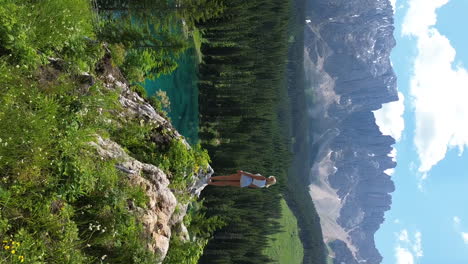 beautiful blonde girl standing on the edge of cliff with a panorama view of lake carezza and dolomite mountains in italy