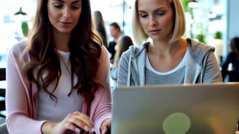 two women are sitting at a table looking at a laptop