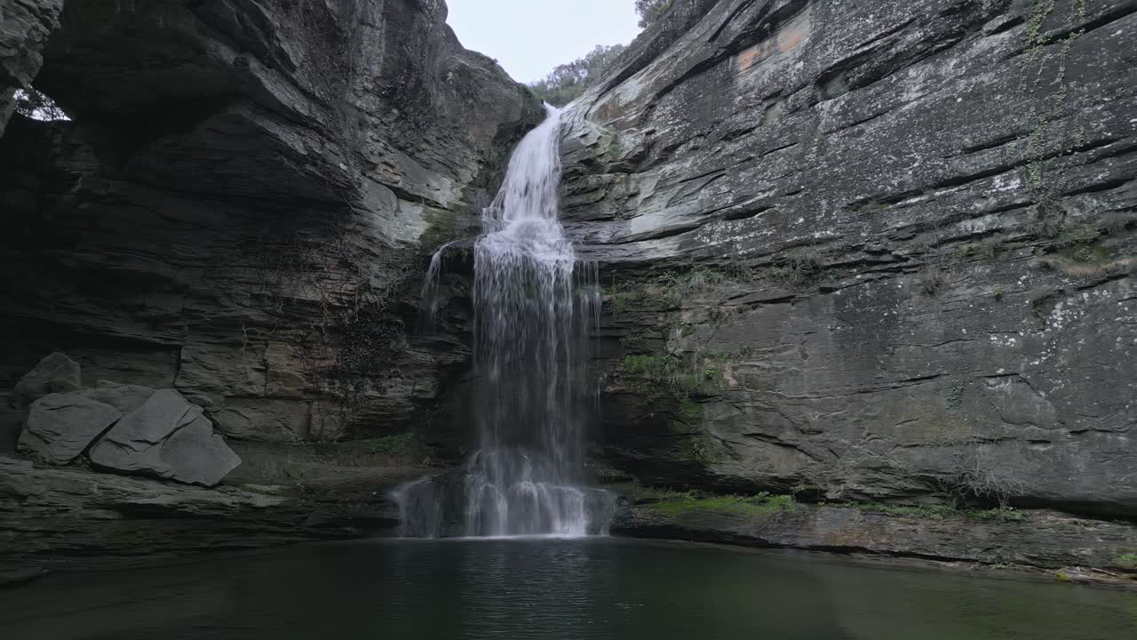 Water flows from La Foradada waterfall and creates a small pond surrounded by rocky cliffs and vegetation in les guilleries, catalonia