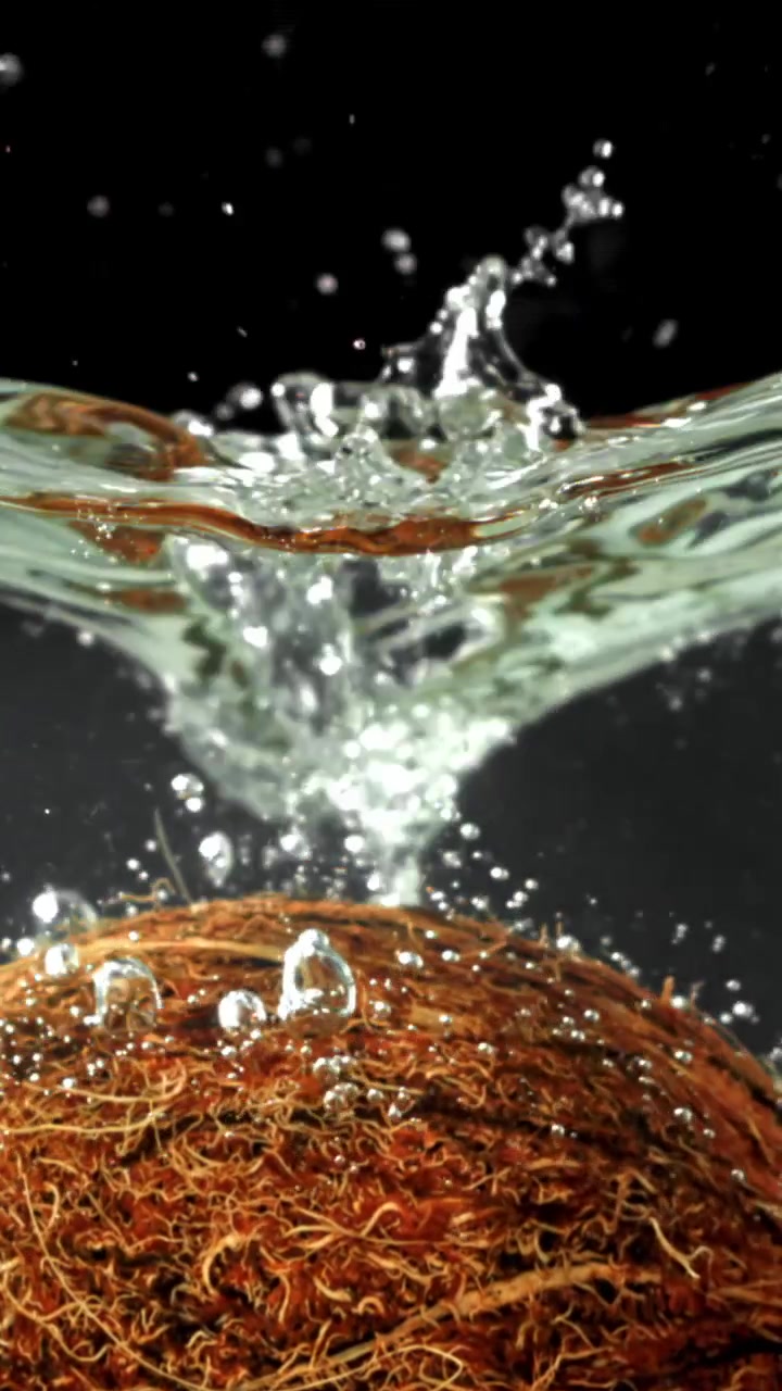 Primo piano di una noce di cocco che schizza nell'acqua con bolle