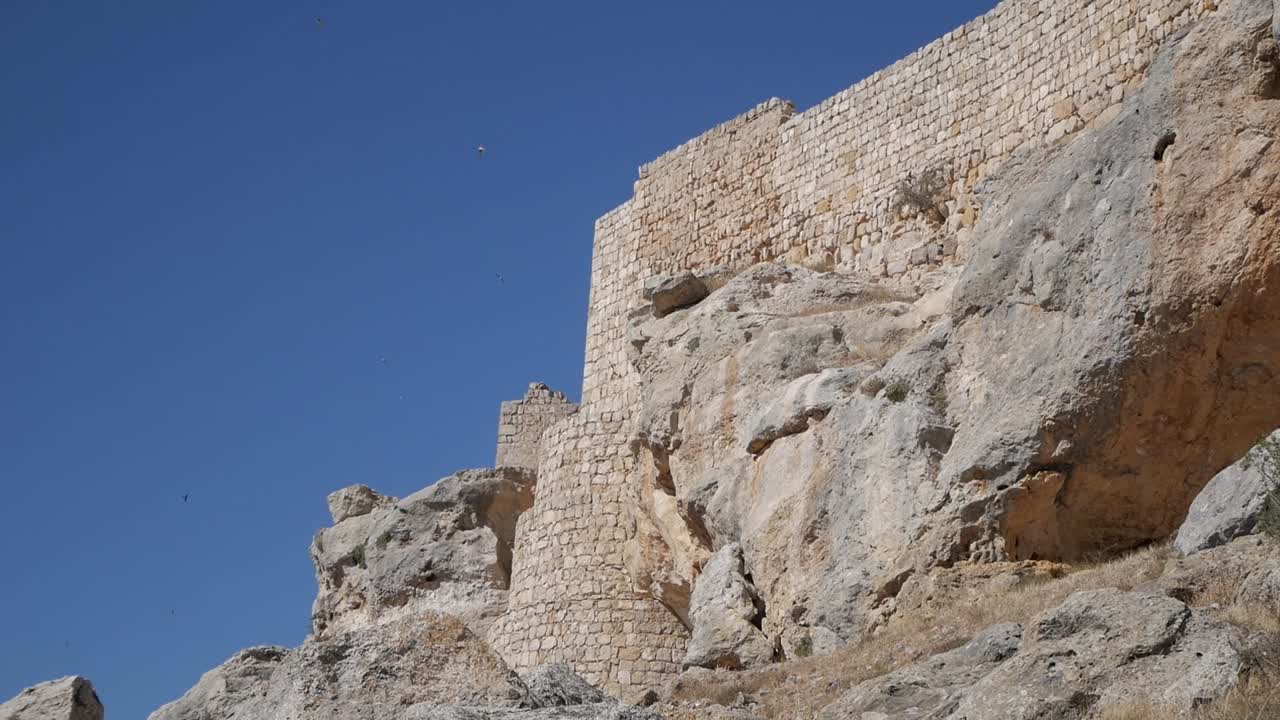 Stone walls of Castillo de Gormaz, standing tall over rocky landscape under clear sky