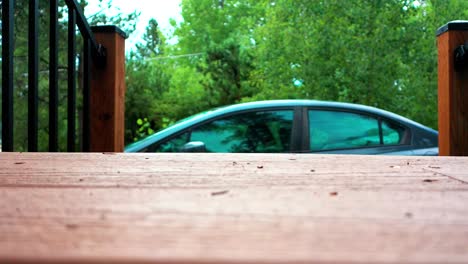 vista de un coche estacionado desde una cubierta de madera en una cabaña en el bosque con un bosque y árboles en el fondo