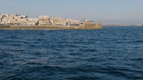 Slow-motion-aerial-footage-flying-over-the-waves-of-the-sea-to-focus-in-on-a-fisherman-off-the-coast-of-Acre,-Israel