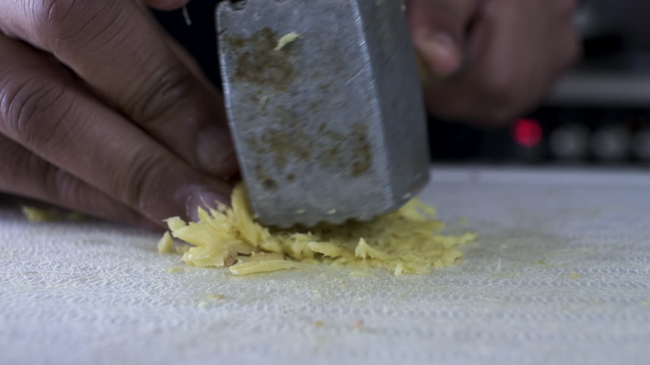 Metal Tenderizer Being Used To Crush Fresh Ginger On Cutting Board