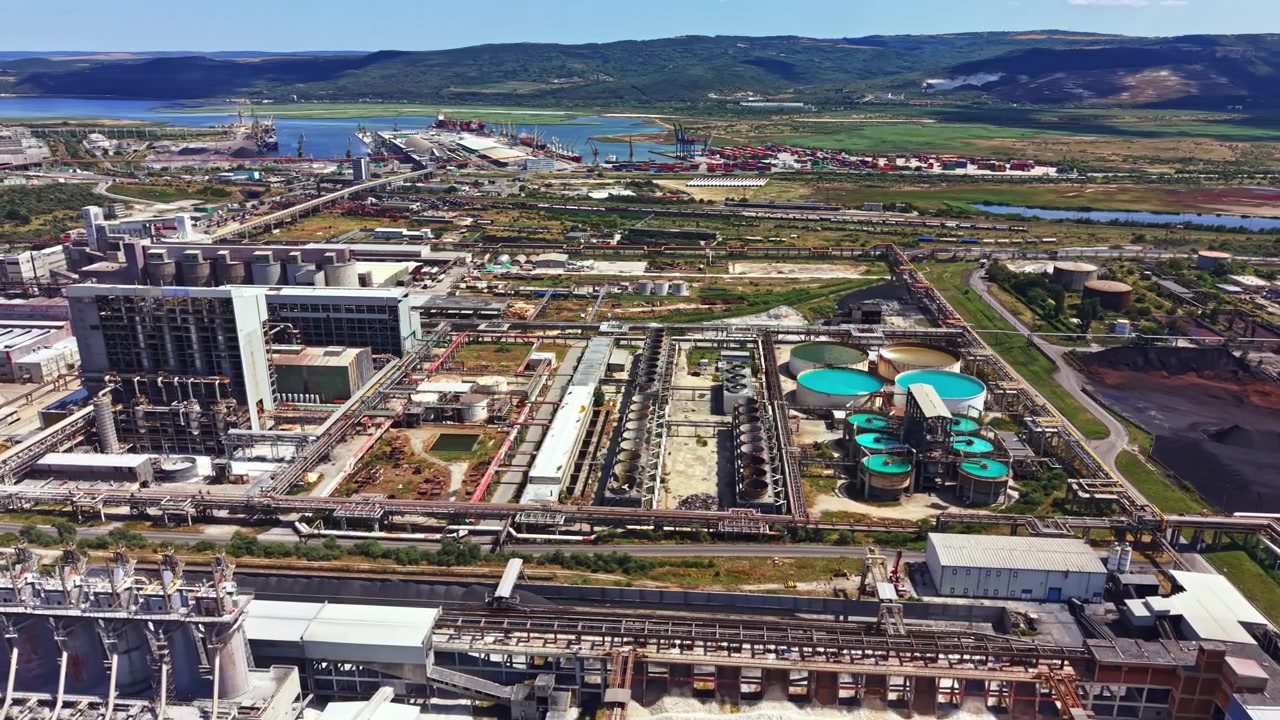 Factory complex located near a river with several industrial buildings, storage facilities, and water treatment ponds visible from above