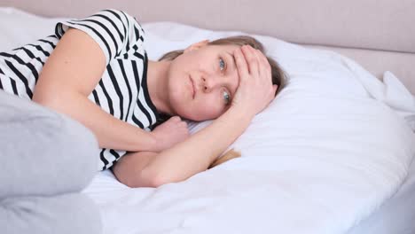A Sad Young Man is Lying in Bed Holding His Head and Has a Headache Human Face Expression of Emotion. A sad young man is lying in bed, holding his head and has a headache. Human face expression of emotion. The girl feels bad and tries to sleep. A woman has a migraine headache