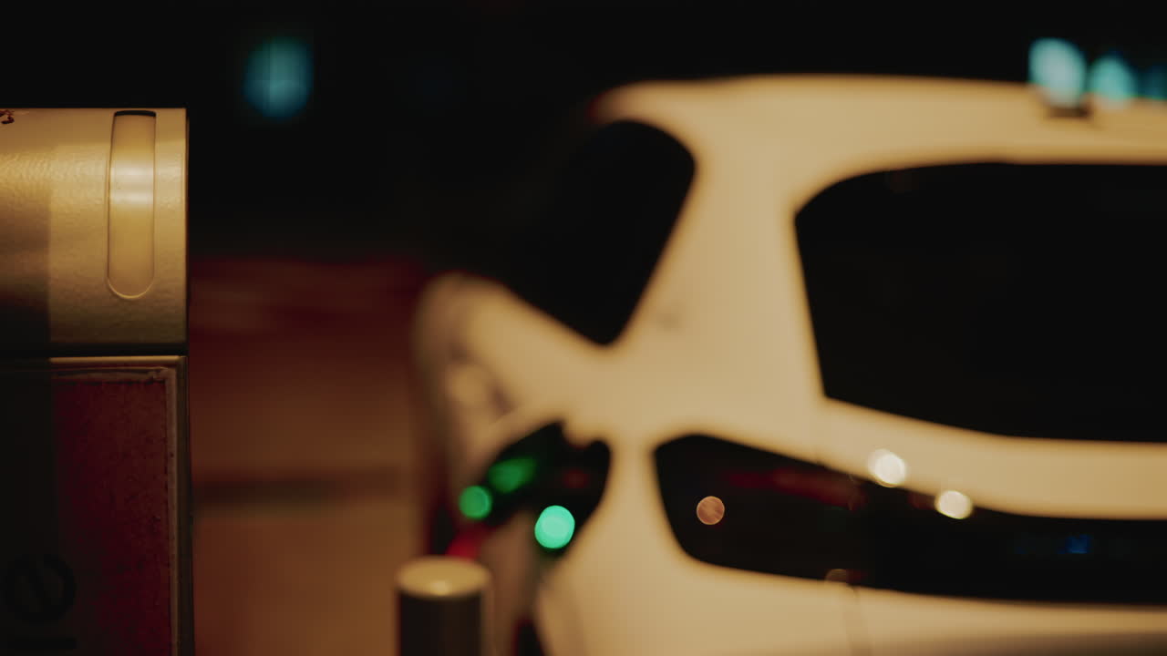Nighttime close up of an illuminated electric charging station next to a white car