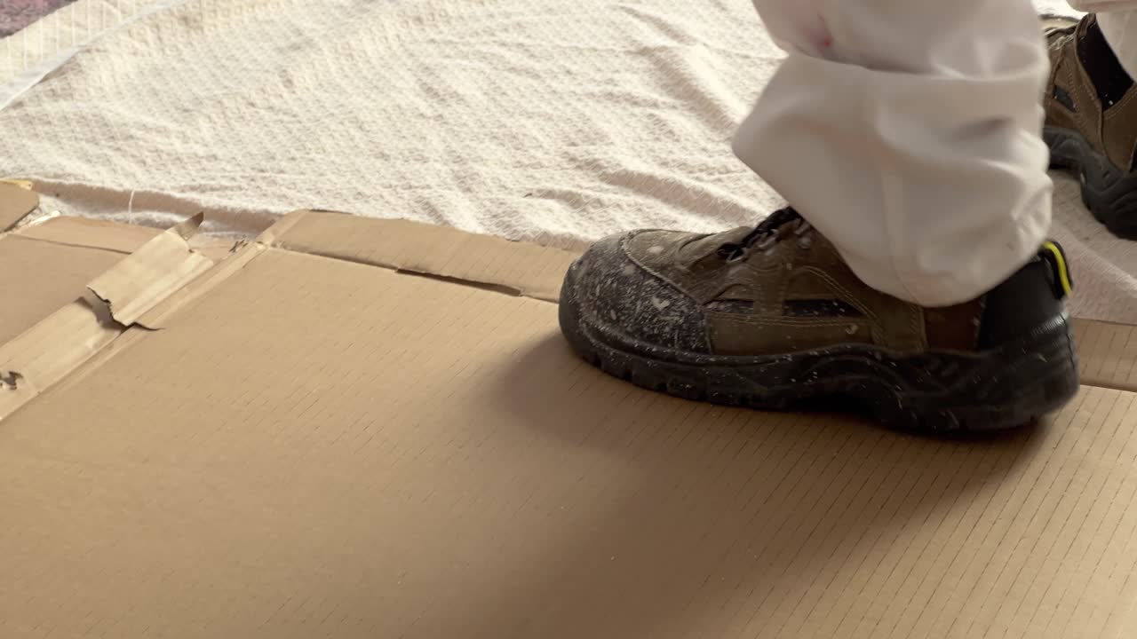 Person is walking over prefabricated paperboard box material, painting the walls, craftsman doing indoor house maintenance and repair concept