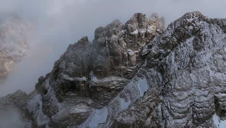 aerial top down shot of icy mountains on mountaintop surrounded by deep clouds at sky