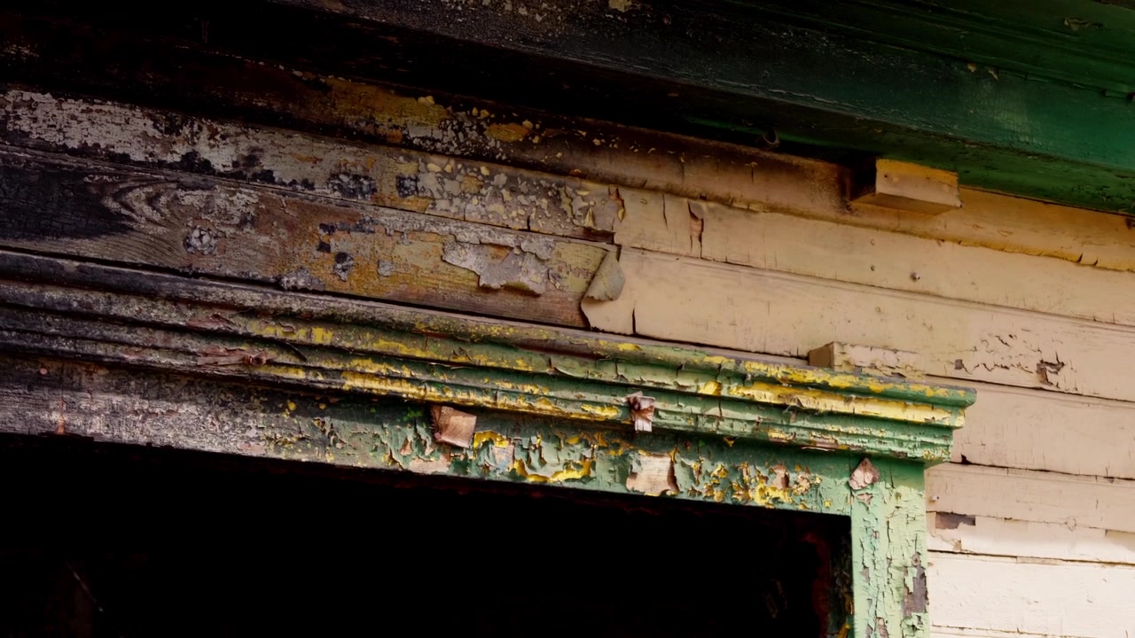 Close up static shot showing severely peeling green and yellow paint on weatherbeaten wooden frame of historic house in Daugavpils, Latvia during sunny summer day.