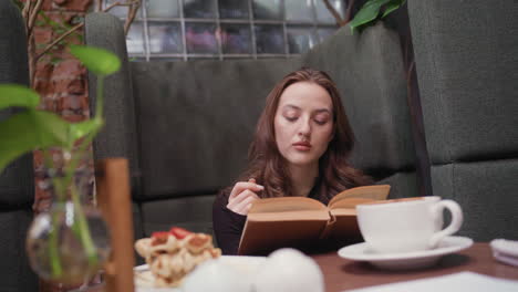 lady in black sits in quiet cozy booth reading brown book while enjoying peaceful moment with waffles and cup of coffee on wooden table surrounded by indoor plants and soft lighting ambiance
