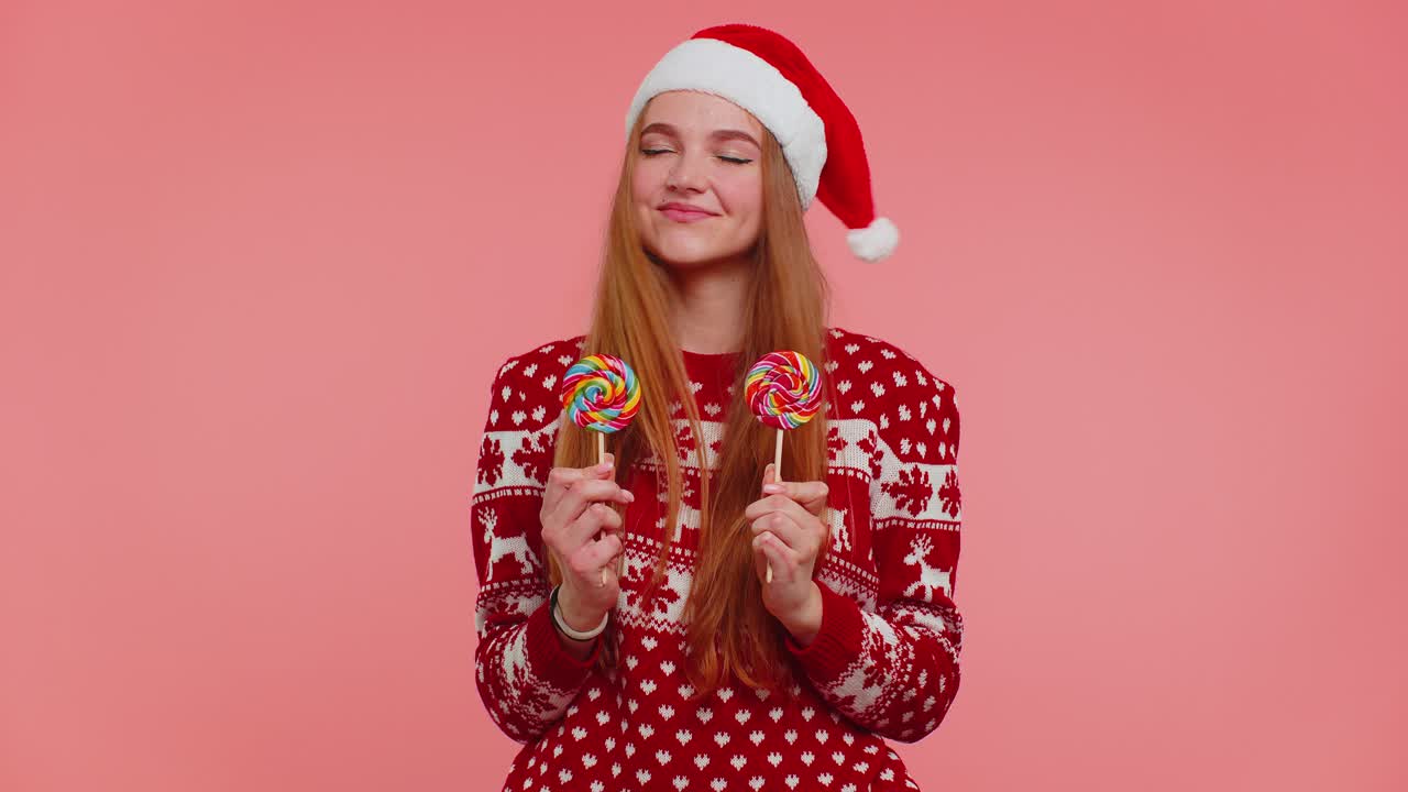 Joyful girl in red christmas sweater hat presenting candy striped lollipops stretches out hands
