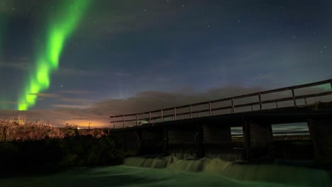 wondrous timelapse of northern lights by the bridge over a flowing river in iceland - static shot