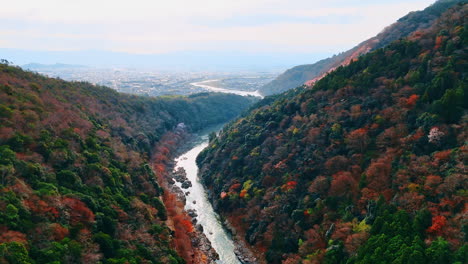 tranquil autumn in the mountains of kyoto, japan. drone footage above the katsura river. cityscape at backdrop.