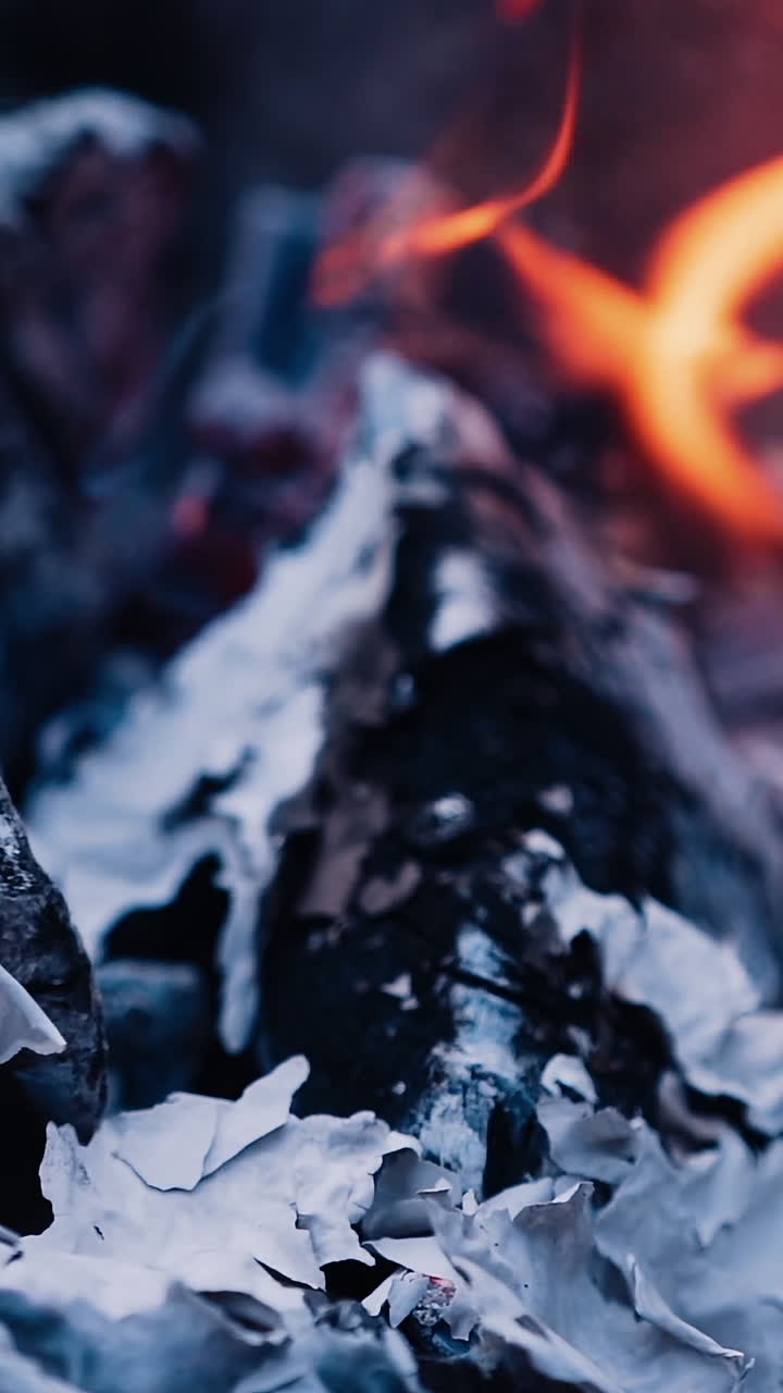 Close-up burning fire with ash. Paper burns on smoldered logs. Smoldering burning logs in fire with ash and coals. Slow motion. Vertical video