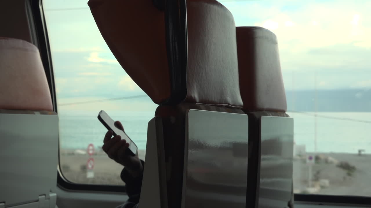Man holding a phone o the window seat of a moving train