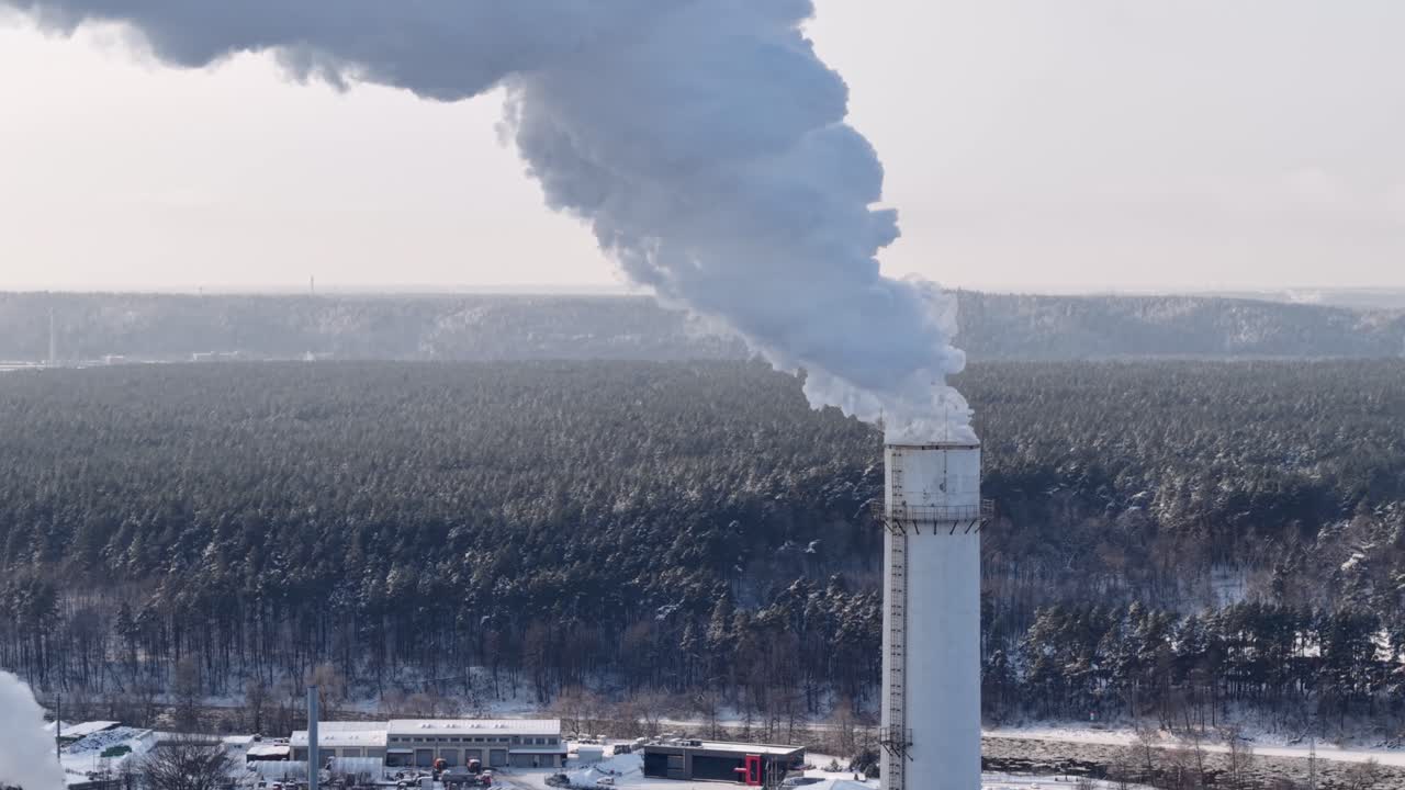Scatto aereo di un'alta ciminiera che rilascia un denso pennacchio di vapore su una foresta innevata vicino a Vilnius, Lituania, che mostra le infrastrutture combinate di calore ed energia e l'inquinamento atmosferico