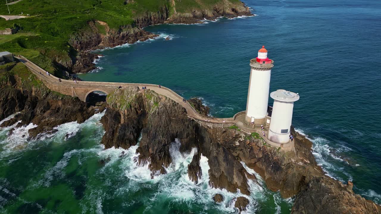 Drone lateral shot revealing the Petit Minou lighthouse from the stone path, with green cliffs in the background and the ocean below. Plouzané. Brittany in France