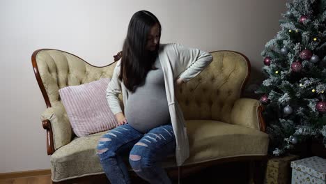 mujer morena embarazada sentada en el sofá durante la navidad con dolor de espalda