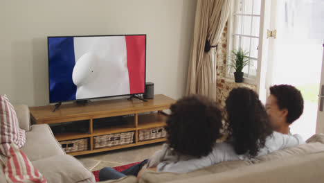 familia biracial viendo la televisión con una pelota de rugby con la bandera de francia en la pantalla