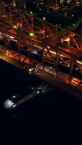 traffic jams on the big bridge at night time. launch going under the bridge along dark river. top view. vertical video