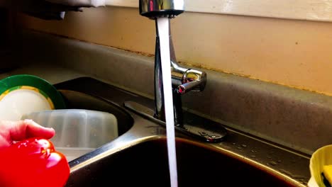 red-bell-peppers-closeup-zoom-in-on-white-man-washing-vegetables-at-kitchen-dual-sink-with-modern-faucet-pouring-out-the-water-while-clean-dishes-are-in-the-second-double-bowl-stainless-steel-design