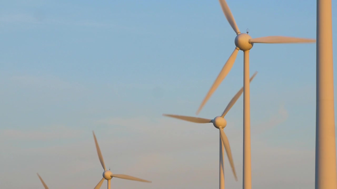 Beautiful view of wind turbines generating renewable energy in the wind farm, green countryside landscape, vibrant sunny spring evening with golden hour light, distant medium wide shot
