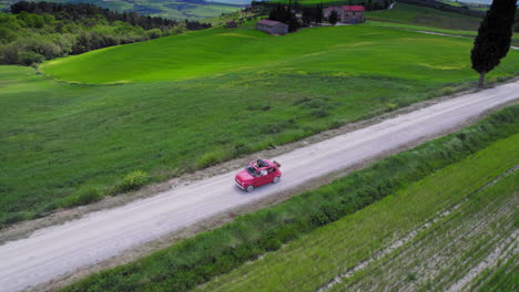 aerial of red car driving on country road in green tuscany landscape