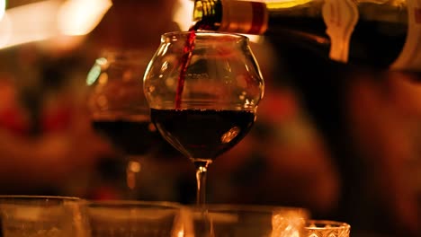 a bottle of red wine is poured into a glass in a warm, ambient dining environment with soft lighting