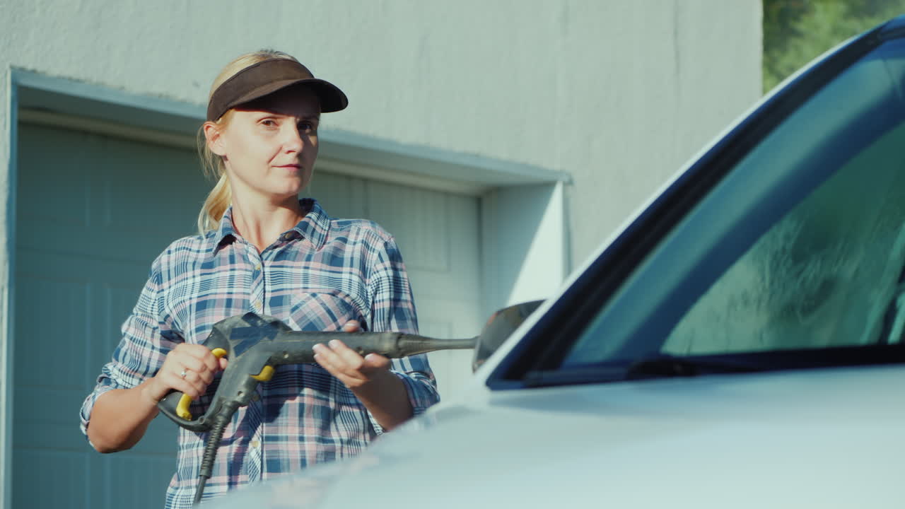 mujer joven lavando su auto cerca del garaje del patio trasero de la casa
