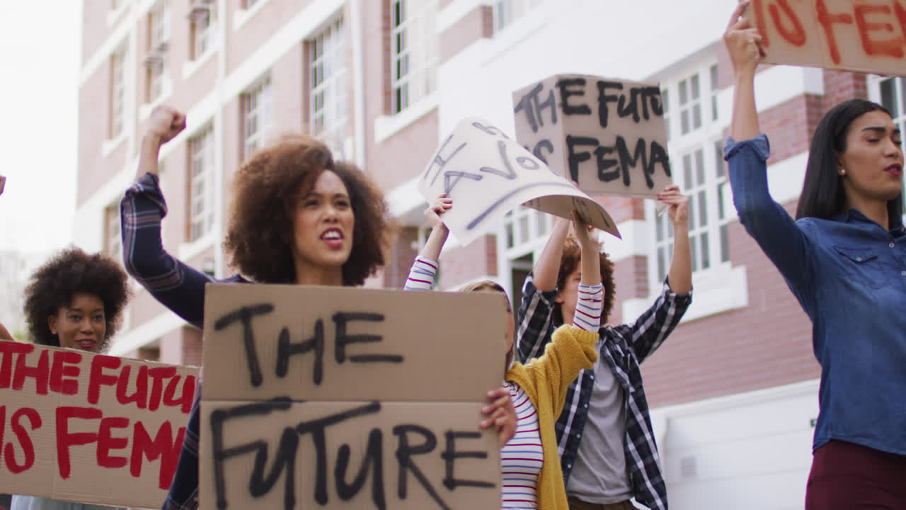 grupo diverso de hombres y mujeres con pancartas levantando puños gritando durante la protesta