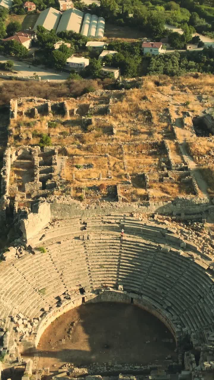 Aerial drone view of tiered stone seating and surrounding ruins at Ancient Theater of Patara in Antalya with warm daylight over aged structure creating strong historic atmosphere for social media