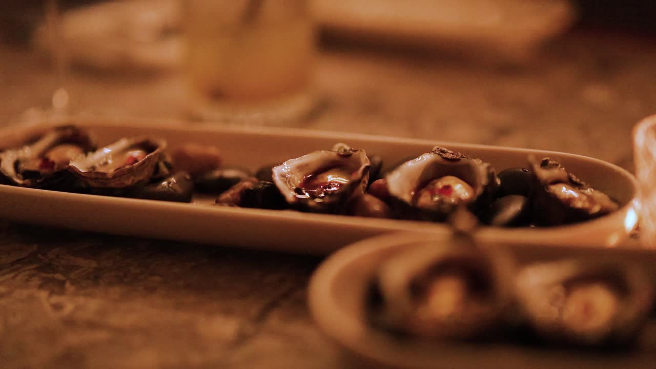 A hand delicately picks oysters from a platter in a warmly lit environment, creating an intimate and cozy atmosphere