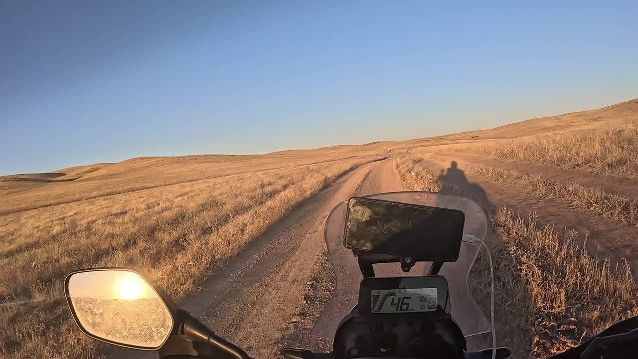 POV Motociclista che guida su un sentiero sterrato al tramonto.