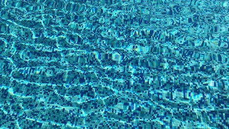crystal clear water in a swimming pool with sunlight casting shadows in the water and on the tiled floor - textured background