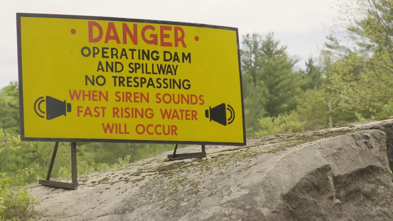 Yellow danger sign next to an hydro electric dam, surrounded by forest
