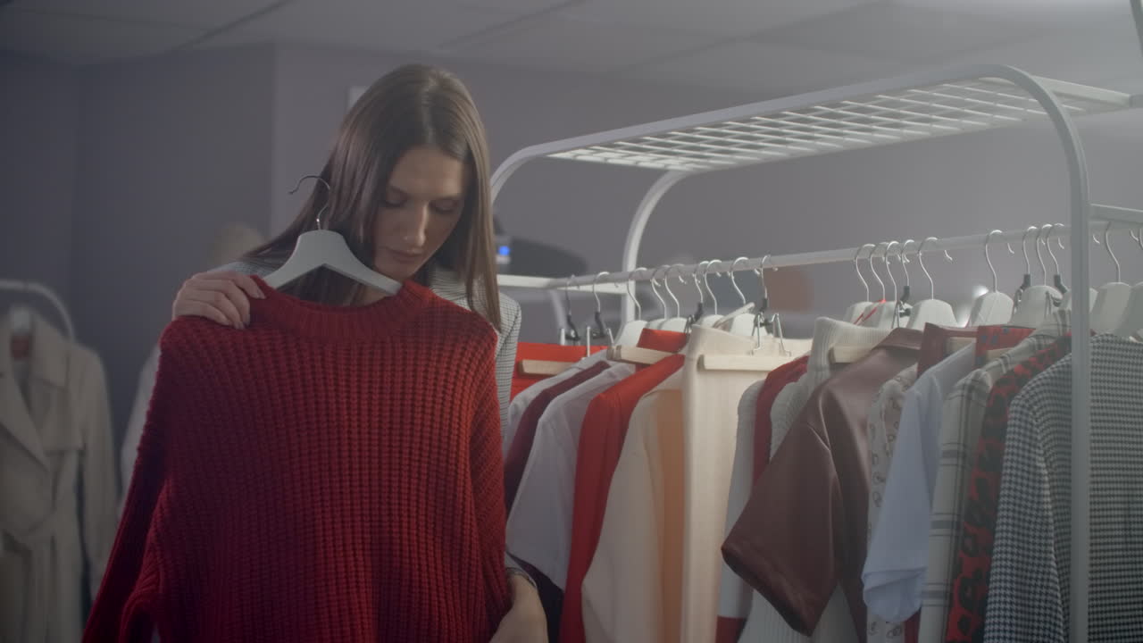 una joven morena en una tienda de ropa elige un vestido para colgar en un colgante y lo prueba. compra un vestido en la tienda. busca y elige ropa en una boutique. toma el vestido del colgante en el soporte